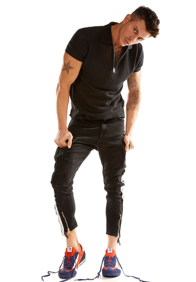 Kenny Braasch modeling a black shirt, black pants, and orange, blue, and white shoes while hunching to the side.