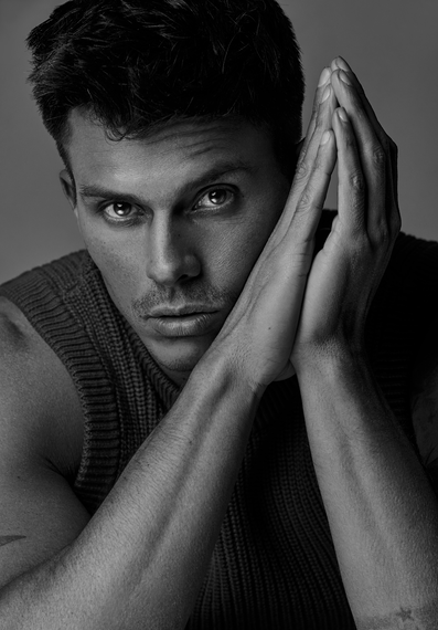 Kenny Braasch modeling sleeveless sweater with hands in prayer position in black and white.